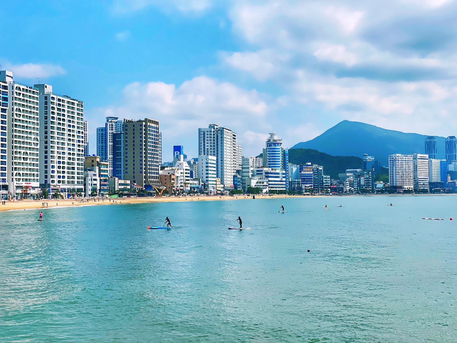 Gwangalli Beach in daylight with paddleboarders and the city behind
